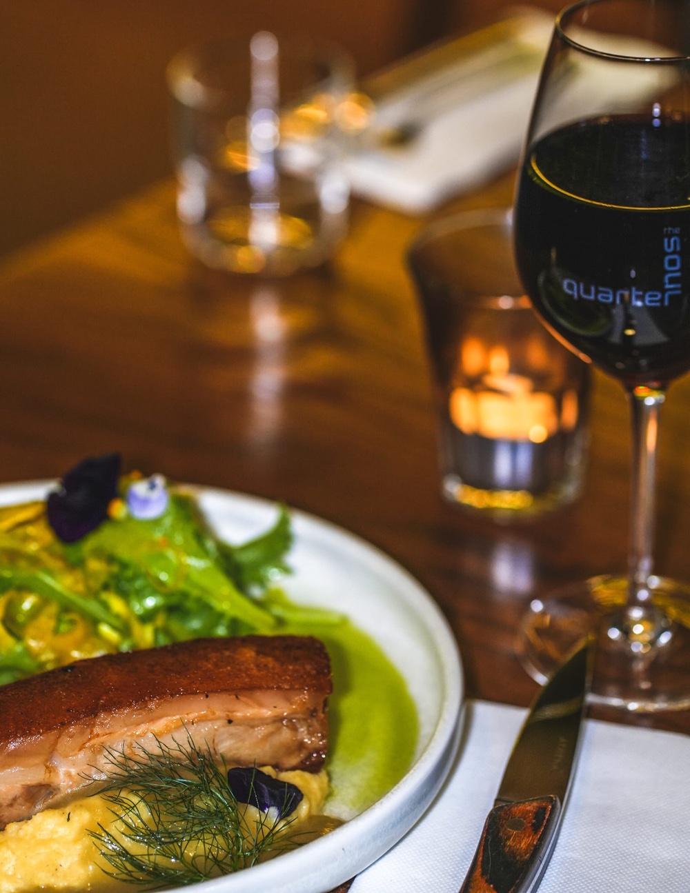 A glass of red wine with pork belly and accompaniments