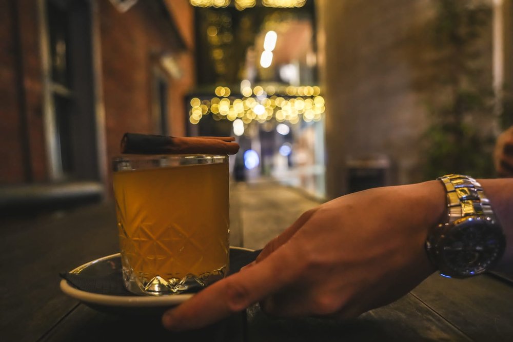 A hand placing a mulled cider in a glass on to a table with a cinnamon stick on top